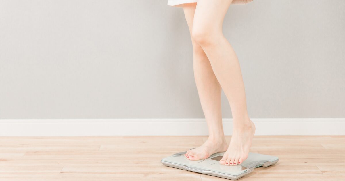 体組成計で体重を測定する女性の全身イメージ